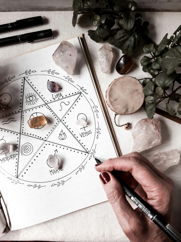 A hand drawing an astrology chart surrounded by crystals and plants, capturing a mystical atmosphere.